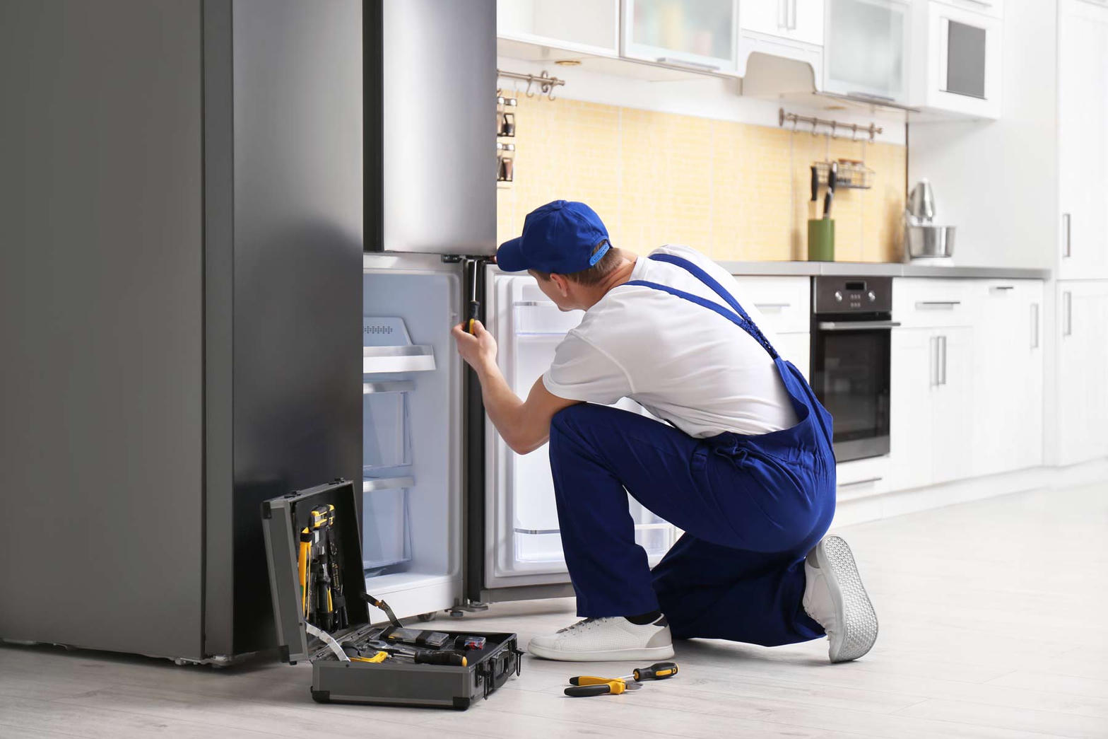 Technician kneeling at an open refrigerator with a toolbox
